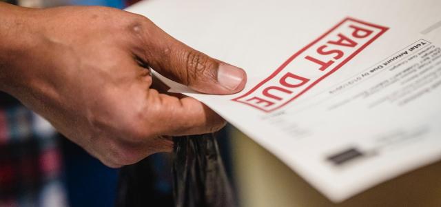 Hand holding a bill with a red "Past Due" stamp on it