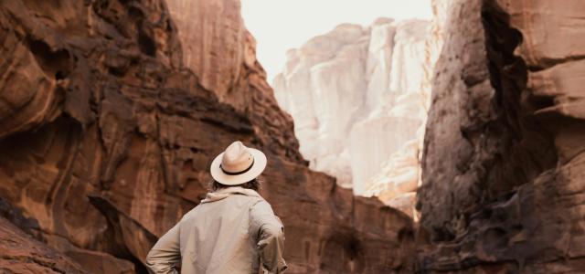 a man in a hat walking through a canyon by NEOM courtesy of Unsplash.